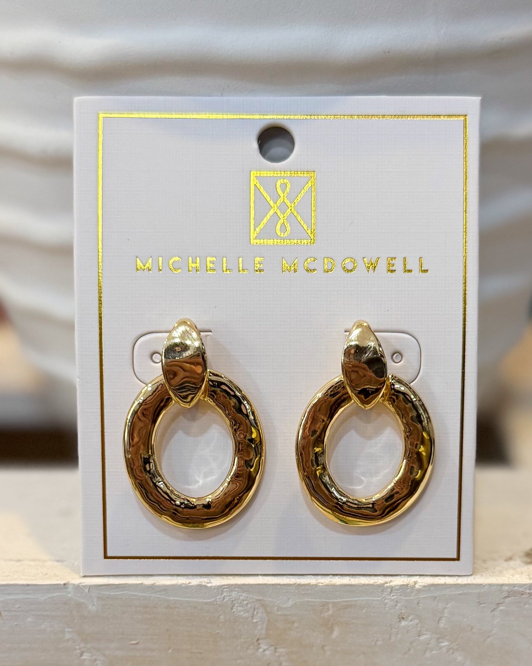 Gold hoop earrings on a branded card with 'Michelle McDowell' logo.