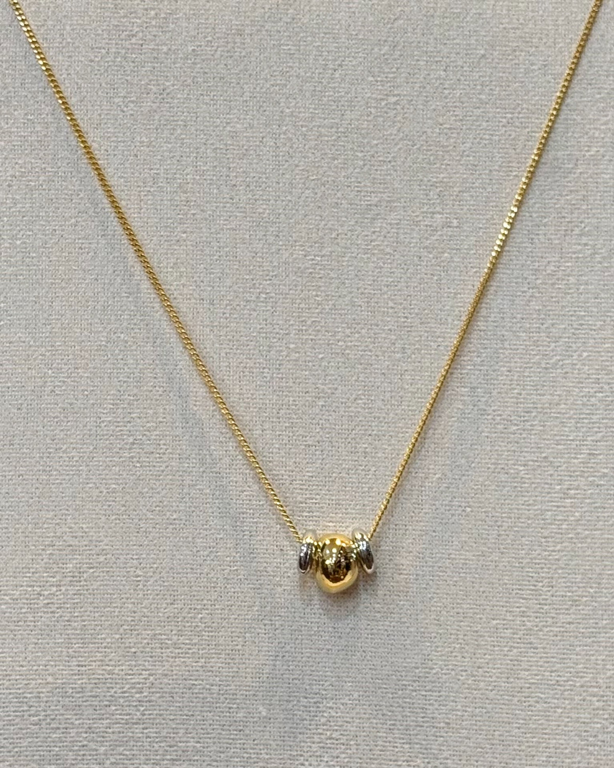 This dainty snake chain necklace features a slim polished chain with two small rounded bead sliders that sit together at the center in two tone finish.
