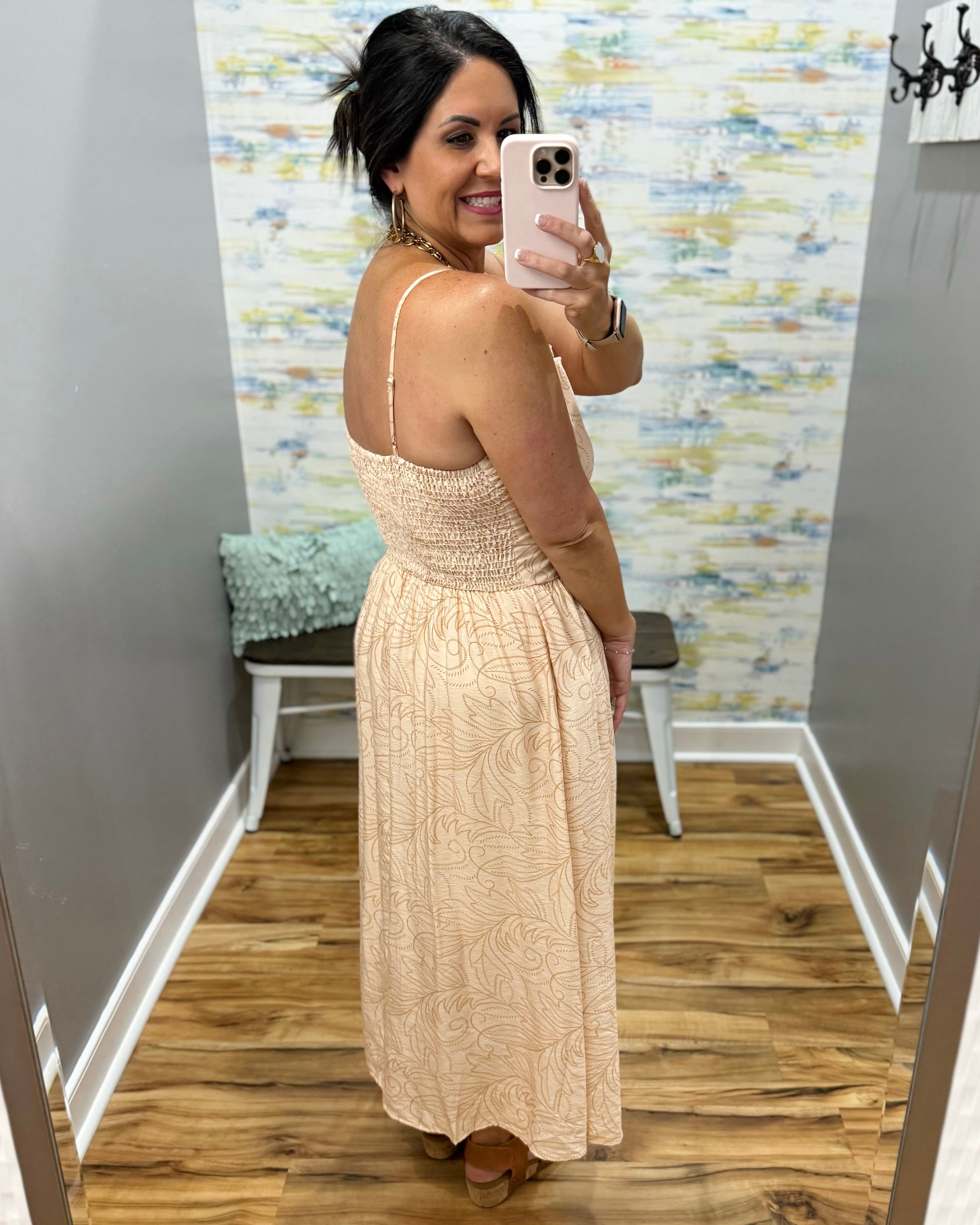 Woman taking a mirror selfie wearing a beige dress in a room with a patterned wall.