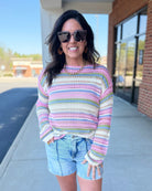 Woman wearing a colorful striped sweater and denim shorts outdoors.