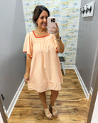 Woman taking a mirror selfie wearing a peach dress with orange trim in a room with patterned wallpaper.