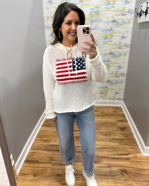 woman wearing american flag knit sweater in white, boyfriend style jeans and white sneakers.