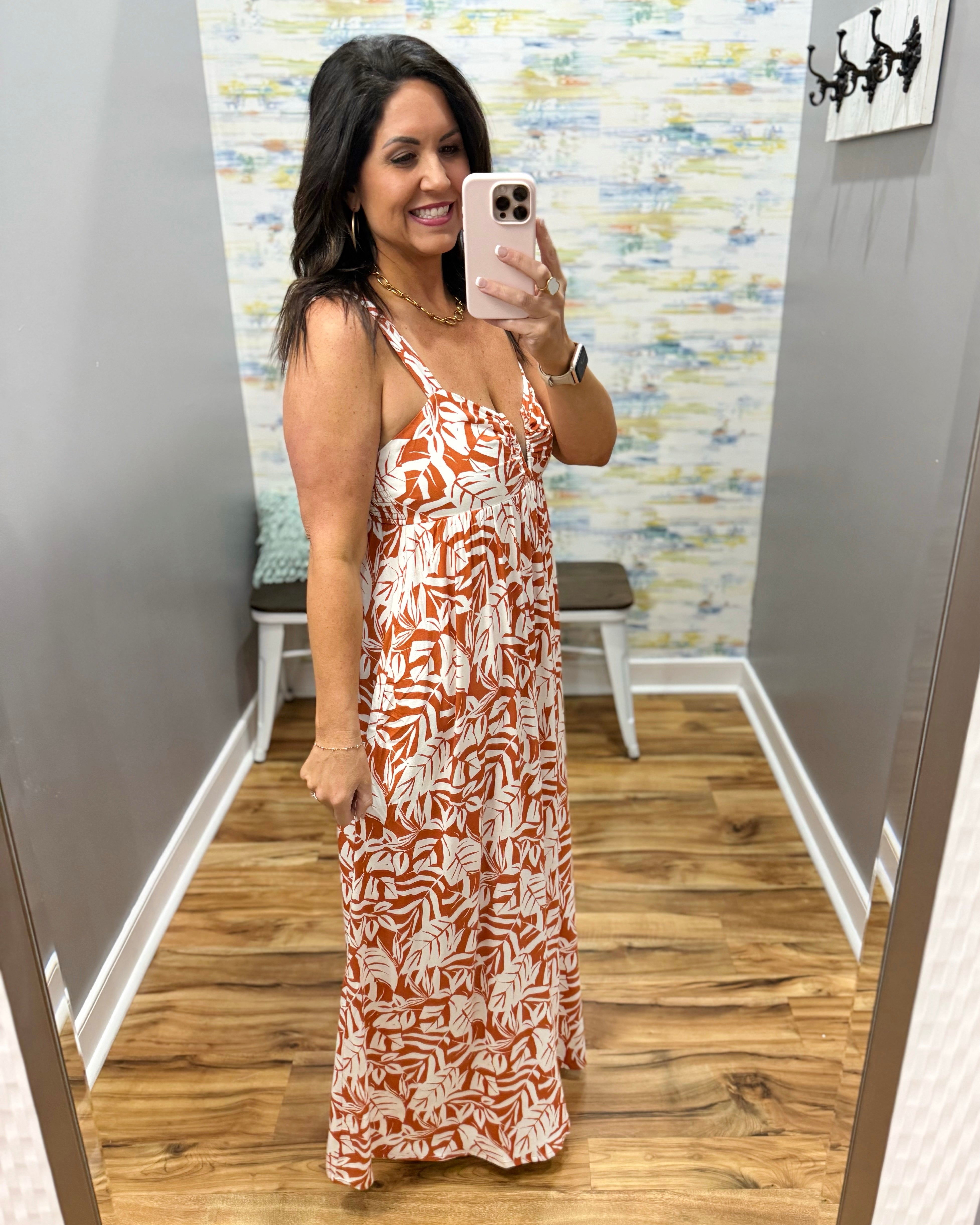 Woman taking a mirror selfie wearing a patterned dress in a room with a colorful wall.