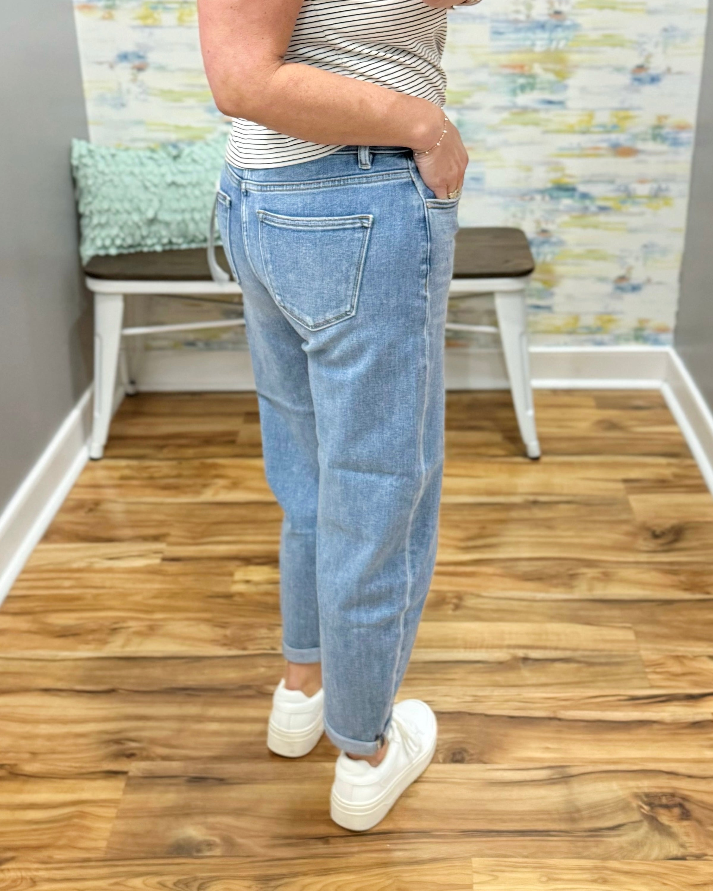 Person wearing light blue jeans and white sneakers in a room with wooden flooring and a colorful wall.