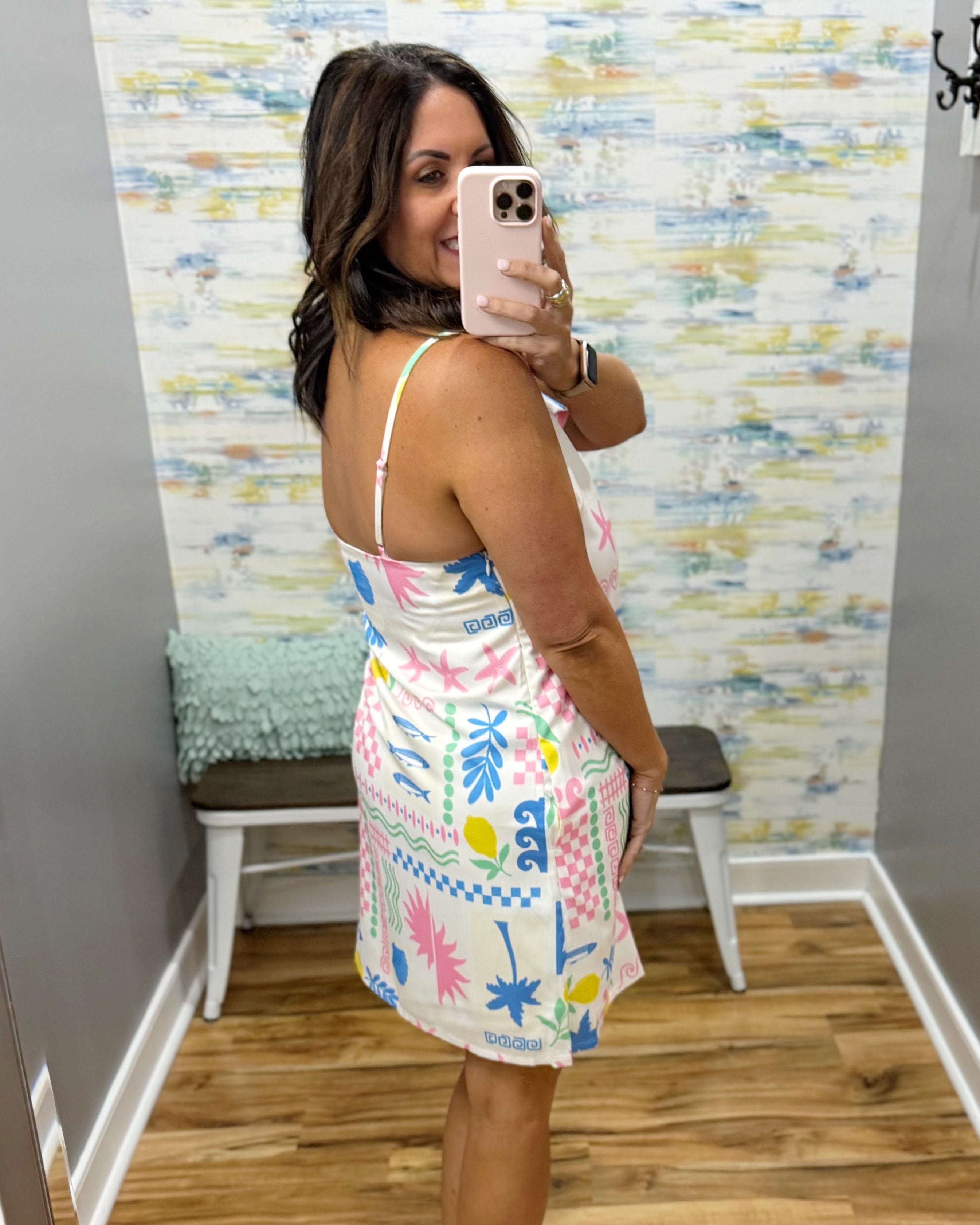 Woman taking a mirror selfie wearing a colorful dress in a room with a patterned wall.