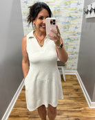 Woman taking a mirror selfie wearing a white dress in a room with a textured wall.