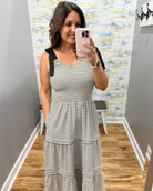Woman taking a mirror selfie wearing a black and white striped dress in a room with a patterned wall.