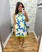 Woman taking a mirror selfie wearing a blue floral dress in a room with a patterned wall.
