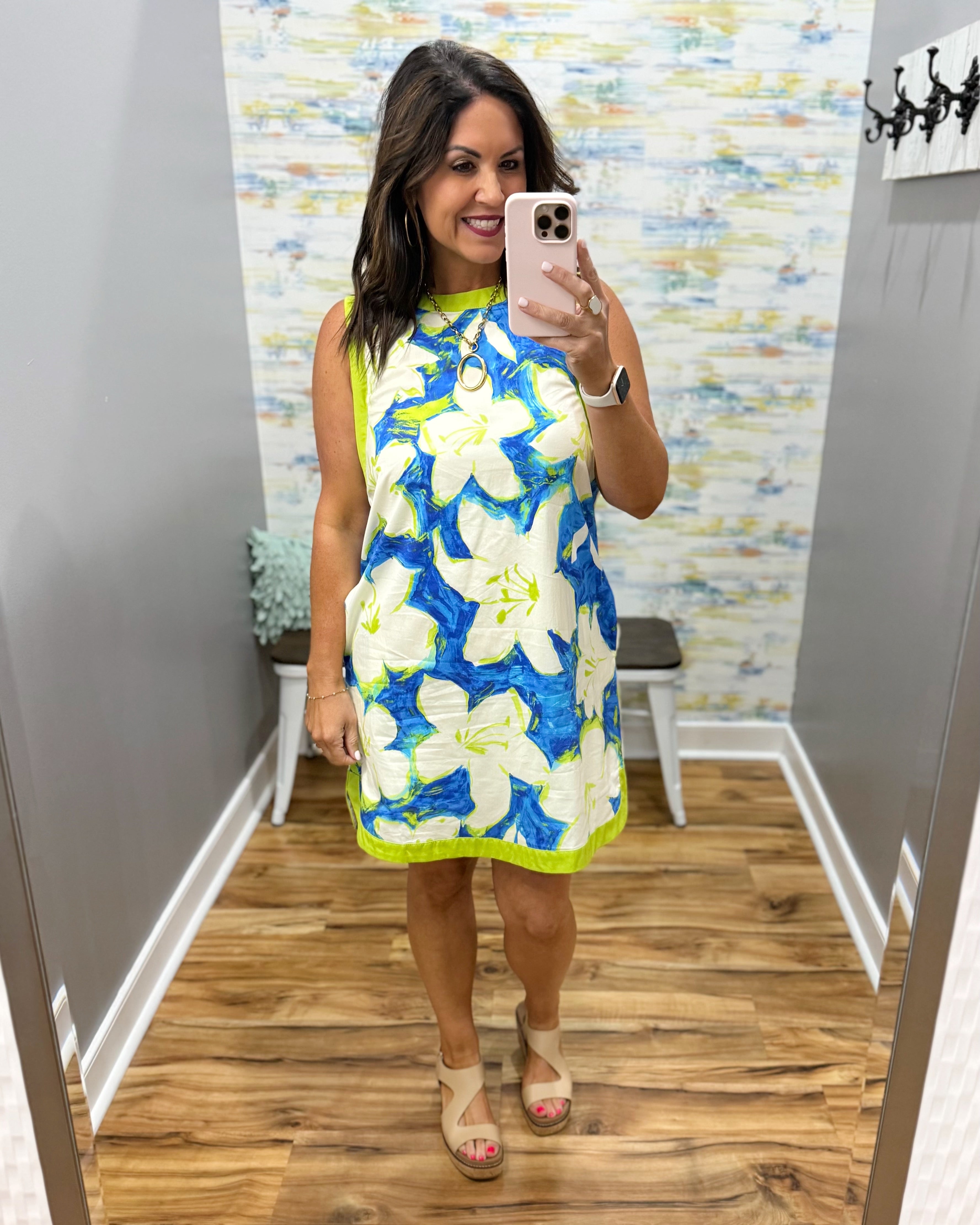 Woman taking a mirror selfie wearing a blue floral dress in a room with a patterned wall.