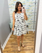Woman taking a mirror selfie wearing a floral dress in a room with a colorful wall.
