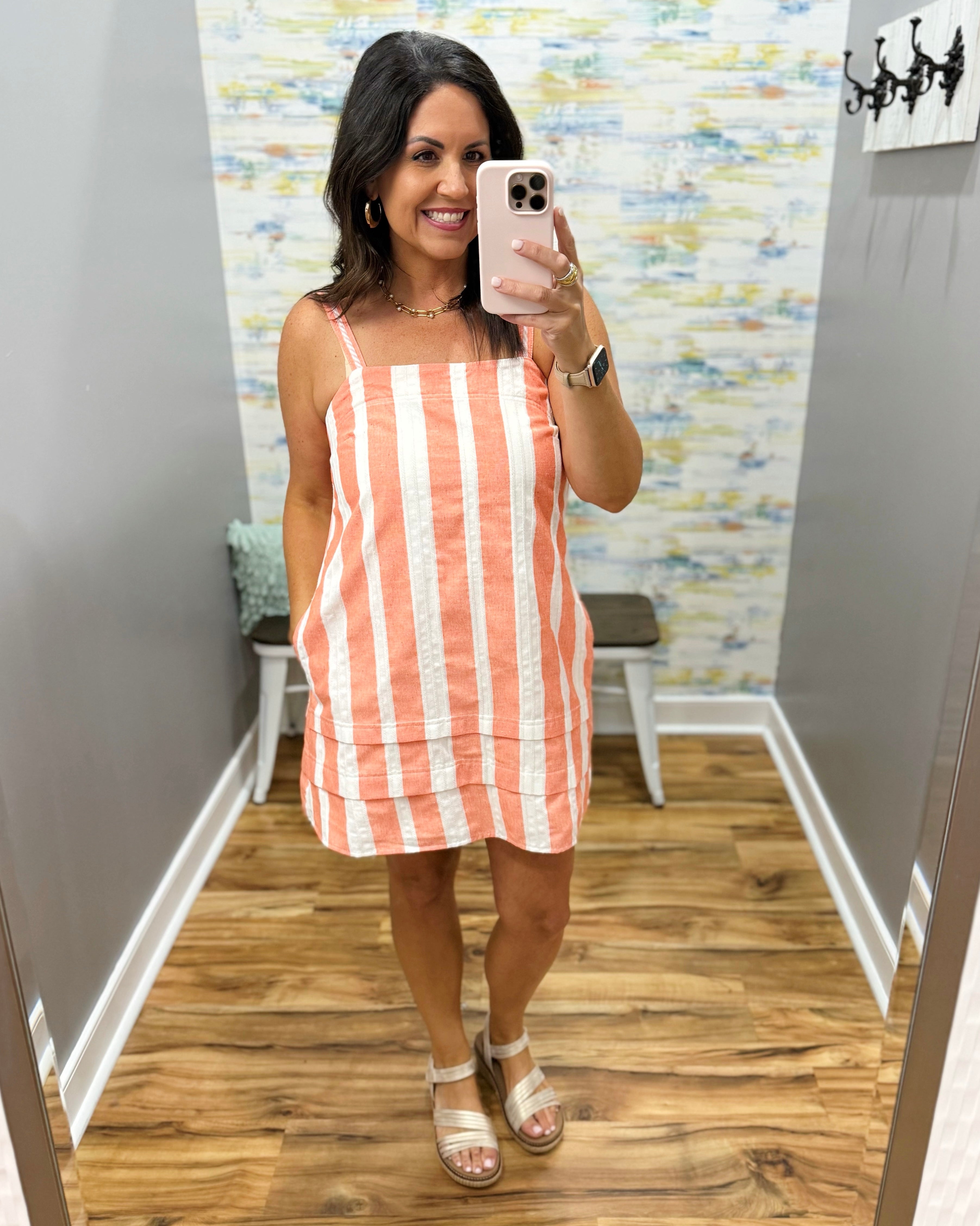 Woman taking a mirror selfie wearing an orange and white striped dress in a room with a patterned wall.
