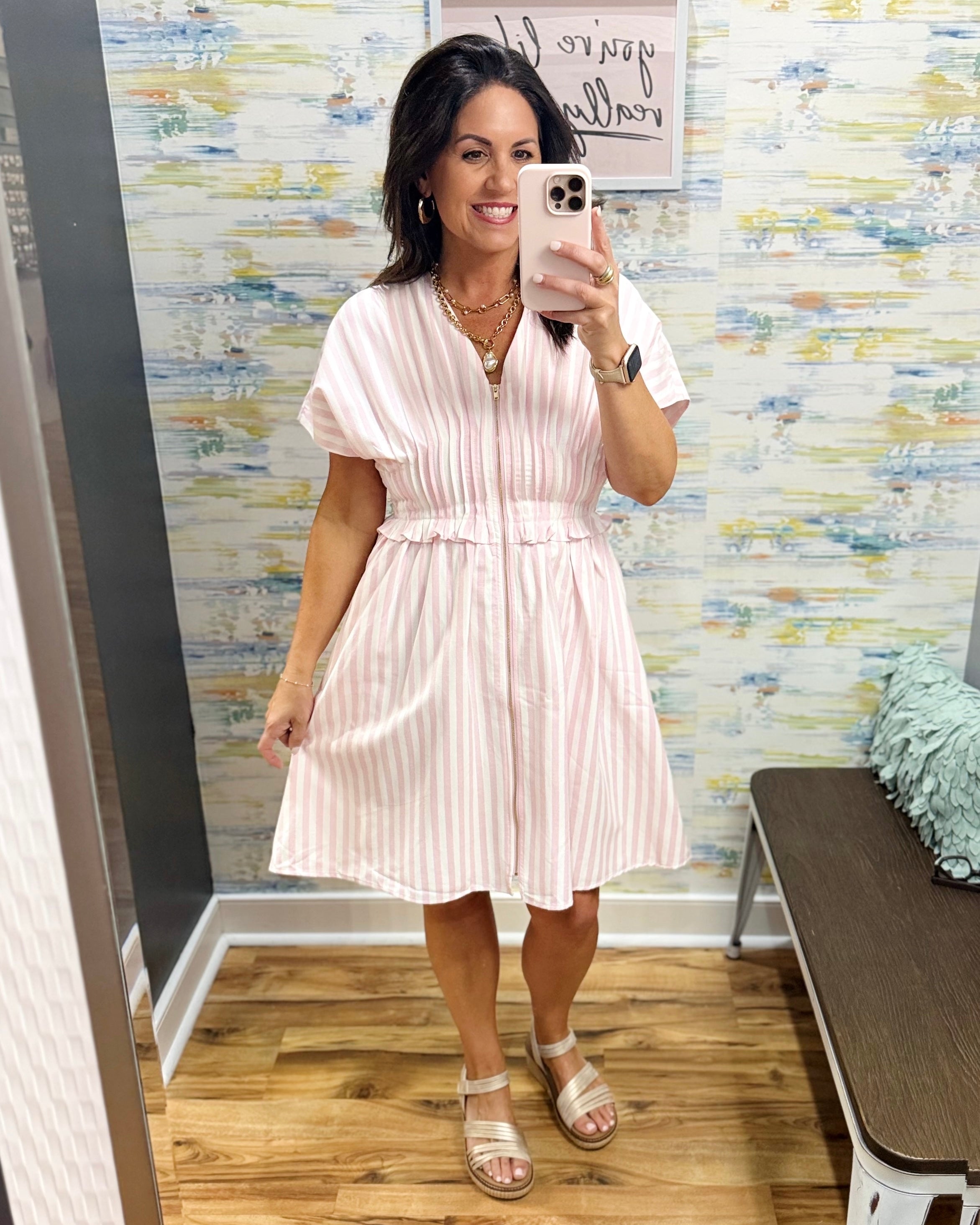 Woman taking a mirror selfie wearing a white dress in a room with colorful wall art.