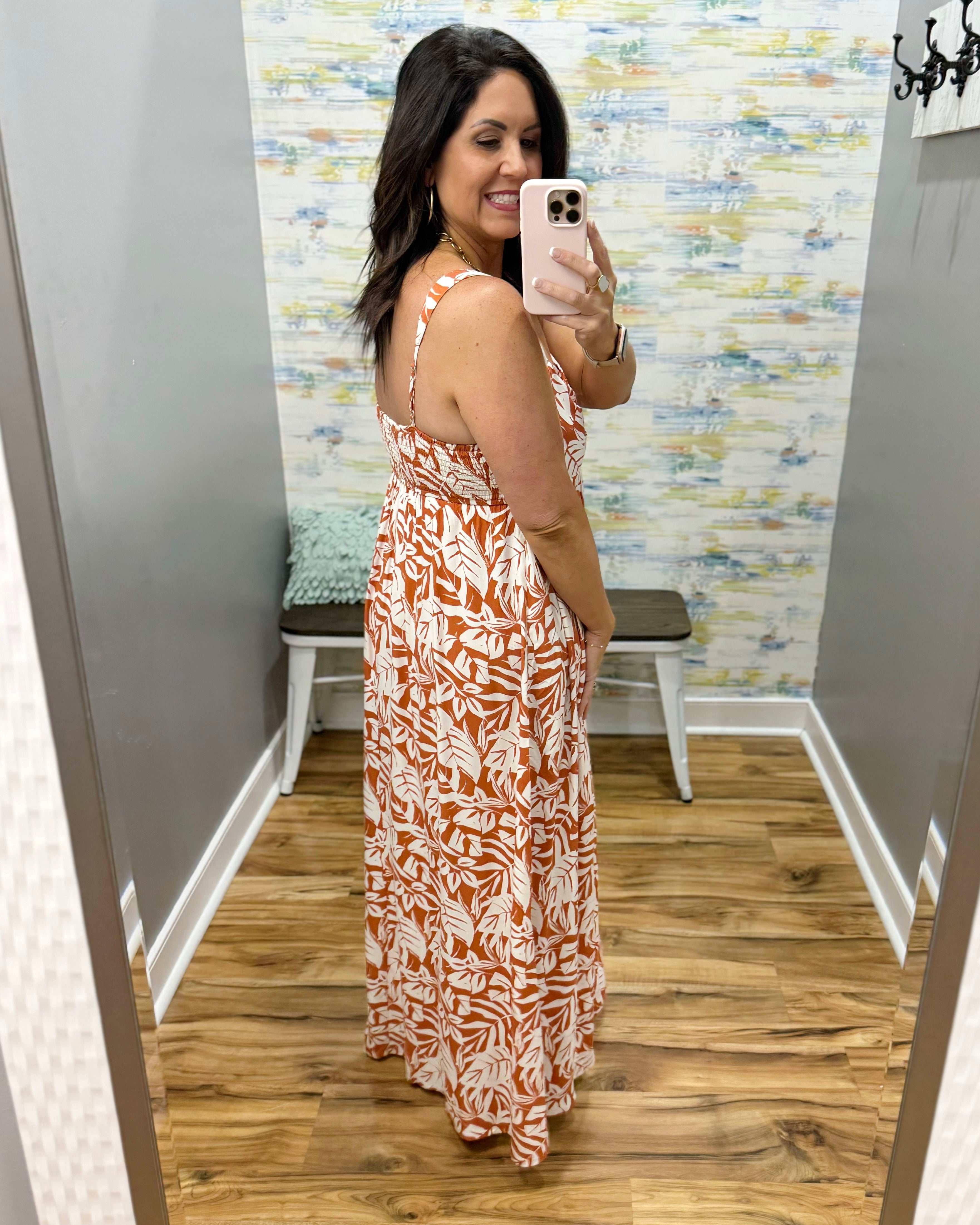 Woman taking a mirror selfie wearing a floral dress in a room with patterned wallpaper.