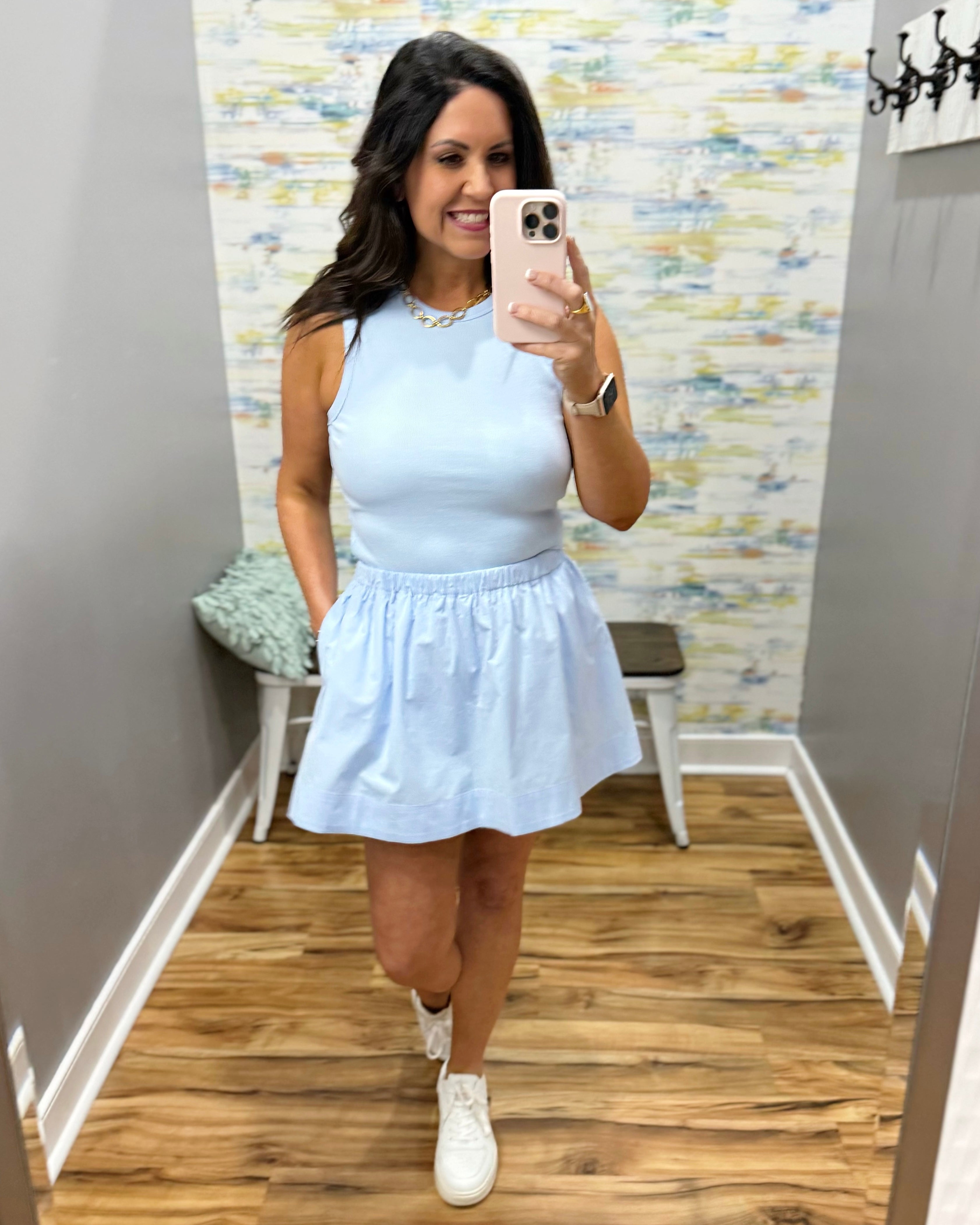 Woman taking a mirror selfie wearing a light blue dress in a room with a patterned wall.