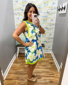 Woman taking a mirror selfie wearing a floral dress in a room with patterned wallpaper.
