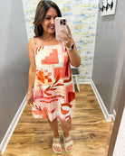 Woman taking a mirror selfie wearing a colorful dress in a room with a patterned wall.