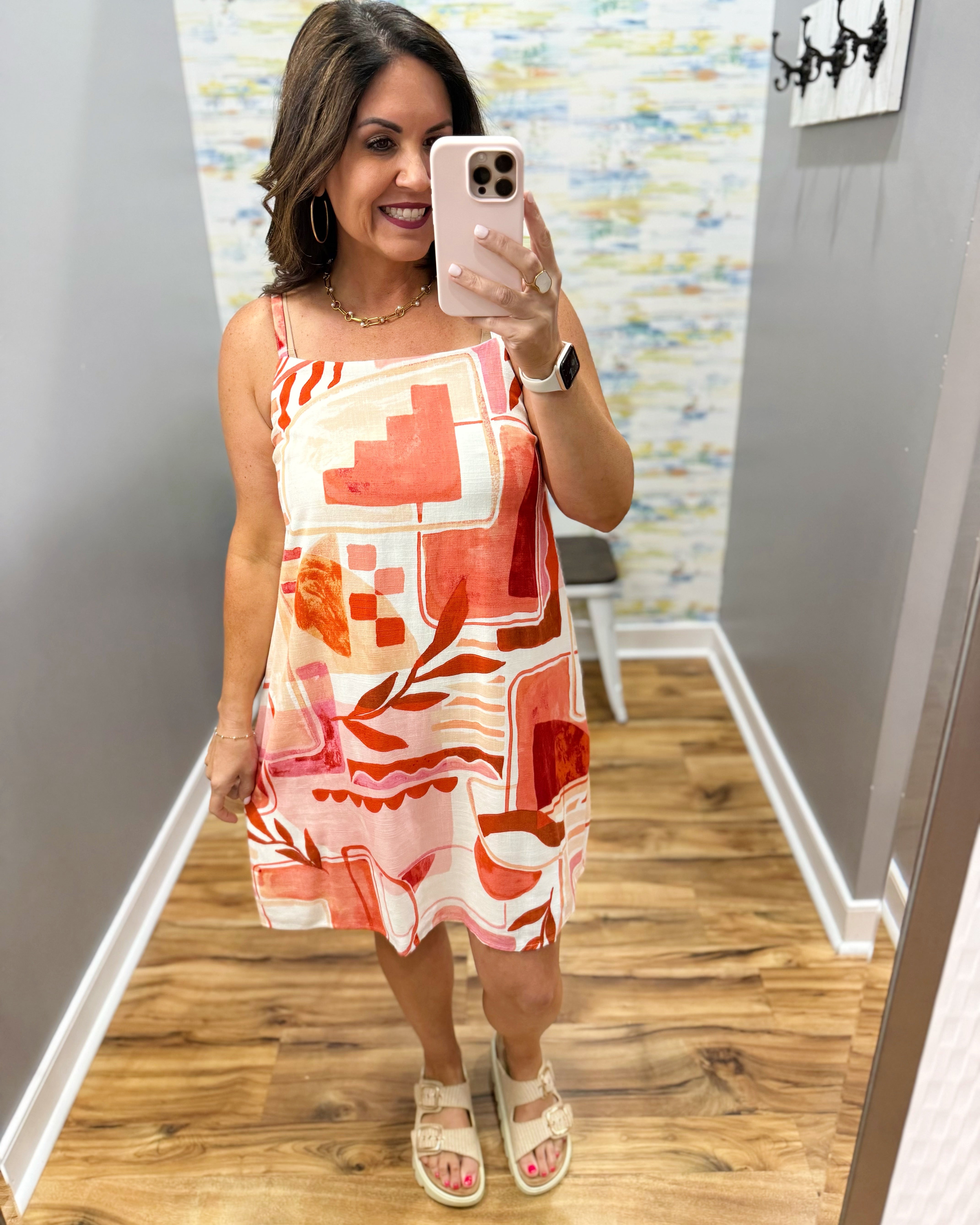 Woman taking a mirror selfie wearing a colorful dress in a room with a patterned wall.