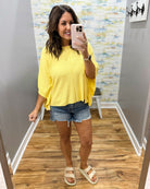 woman wearing a yellow dolman sleeve top with denim shorts.