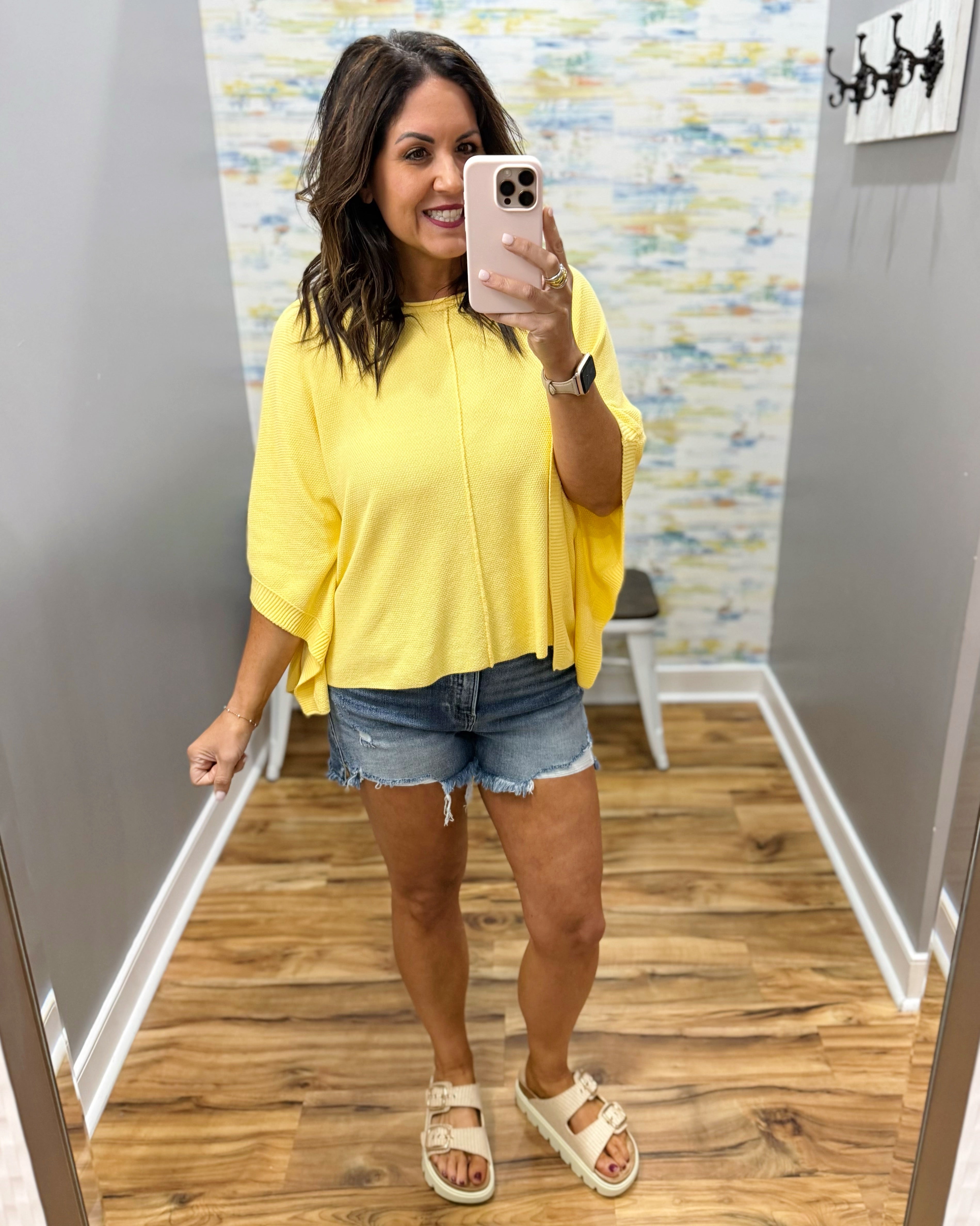 woman wearing a yellow dolman sleeve top with denim shorts.
