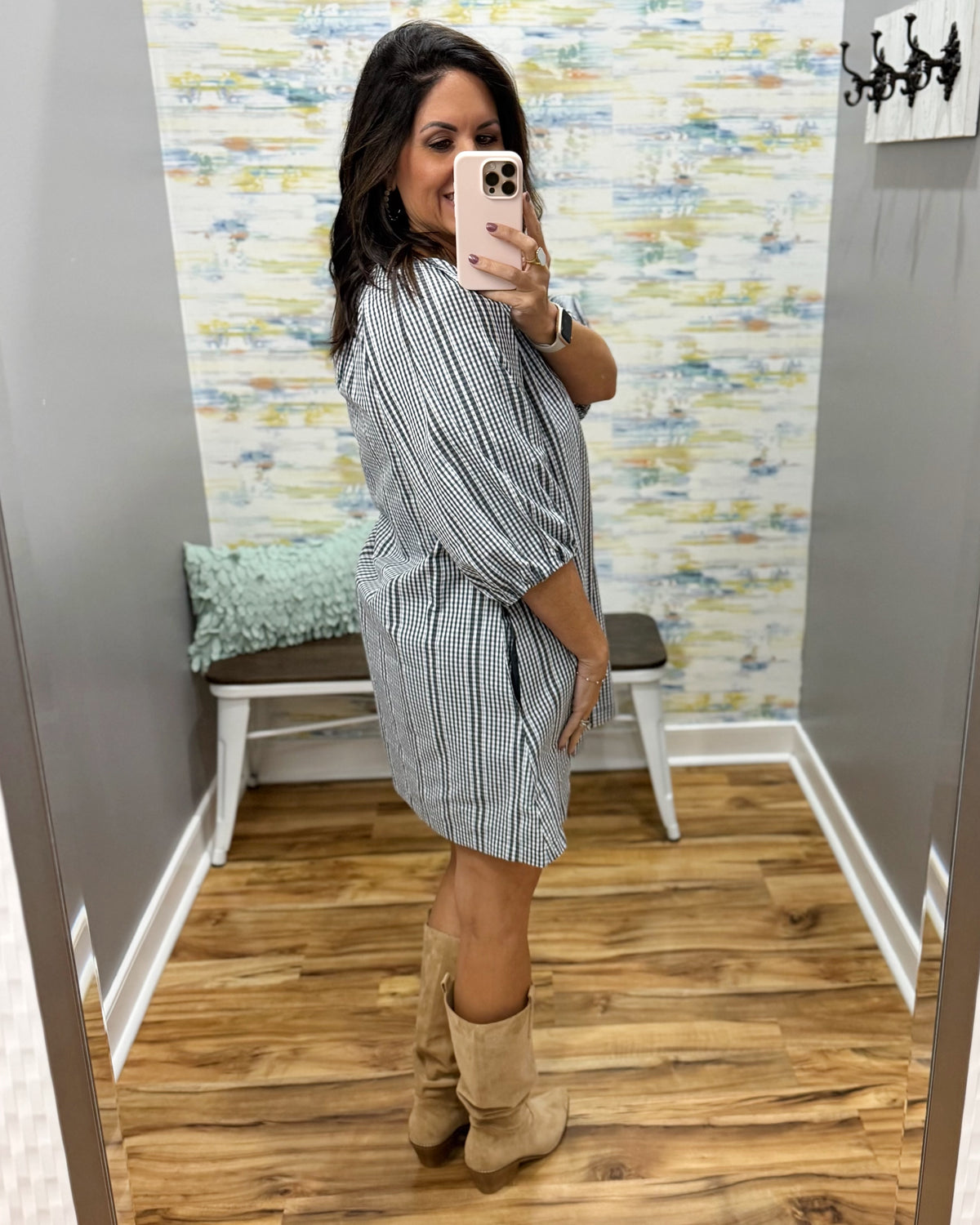 A woman takes a mirror selfie in a fitting room wearing a short black and white vertically striped shirt dress with elbow-length puff sleeves and tan suede boots.