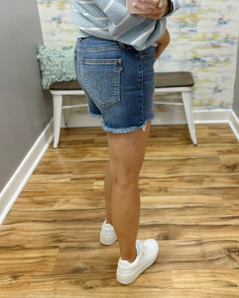 Person wearing blue denim shorts and white sneakers on a wooden floor.