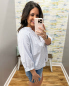Woman taking a mirror selfie wearing a white striped shirt and denim shorts in a room with a colorful wall.