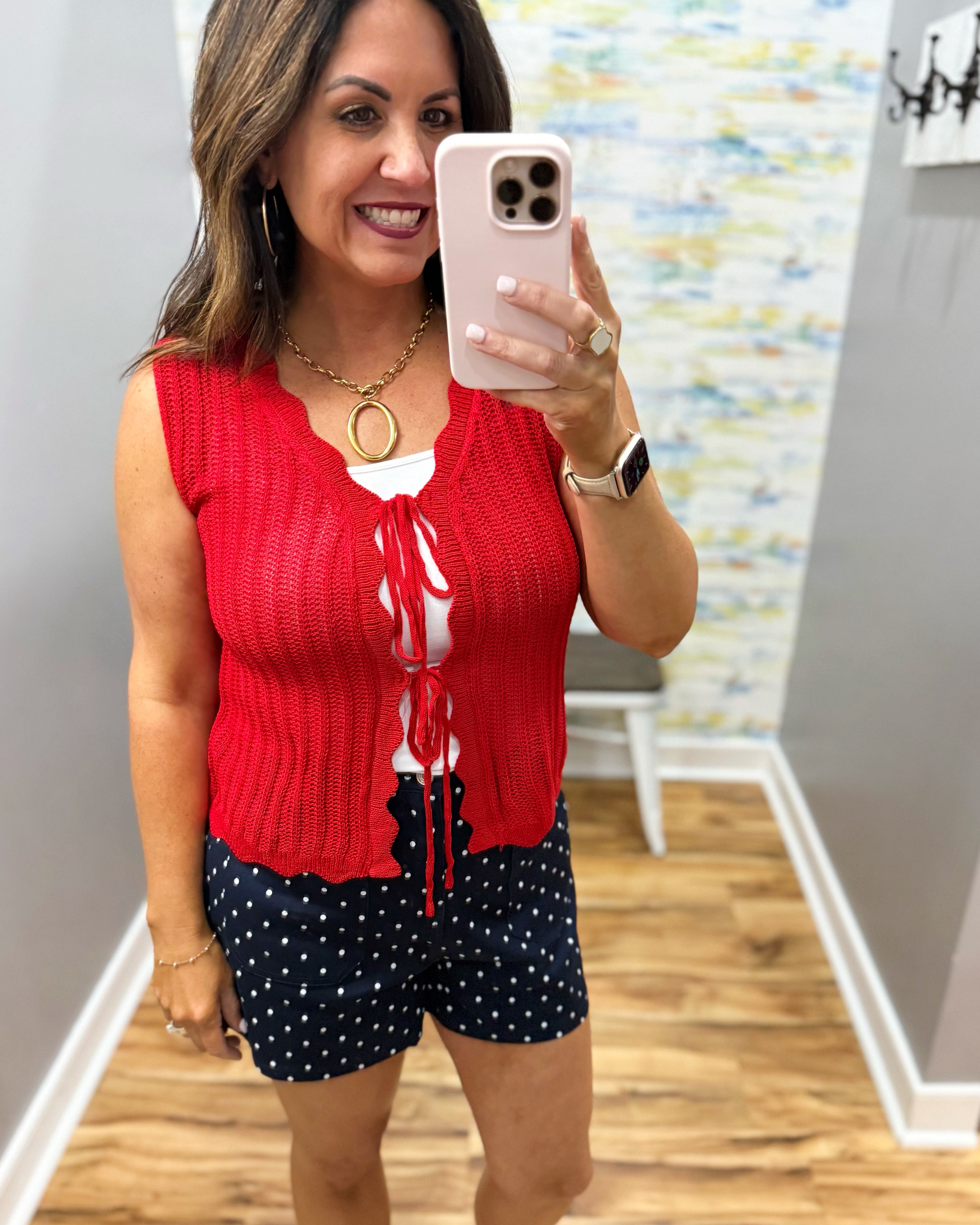 Woman taking a mirror selfie wearing a red sleeveless top and navy shorts with white polka dots.