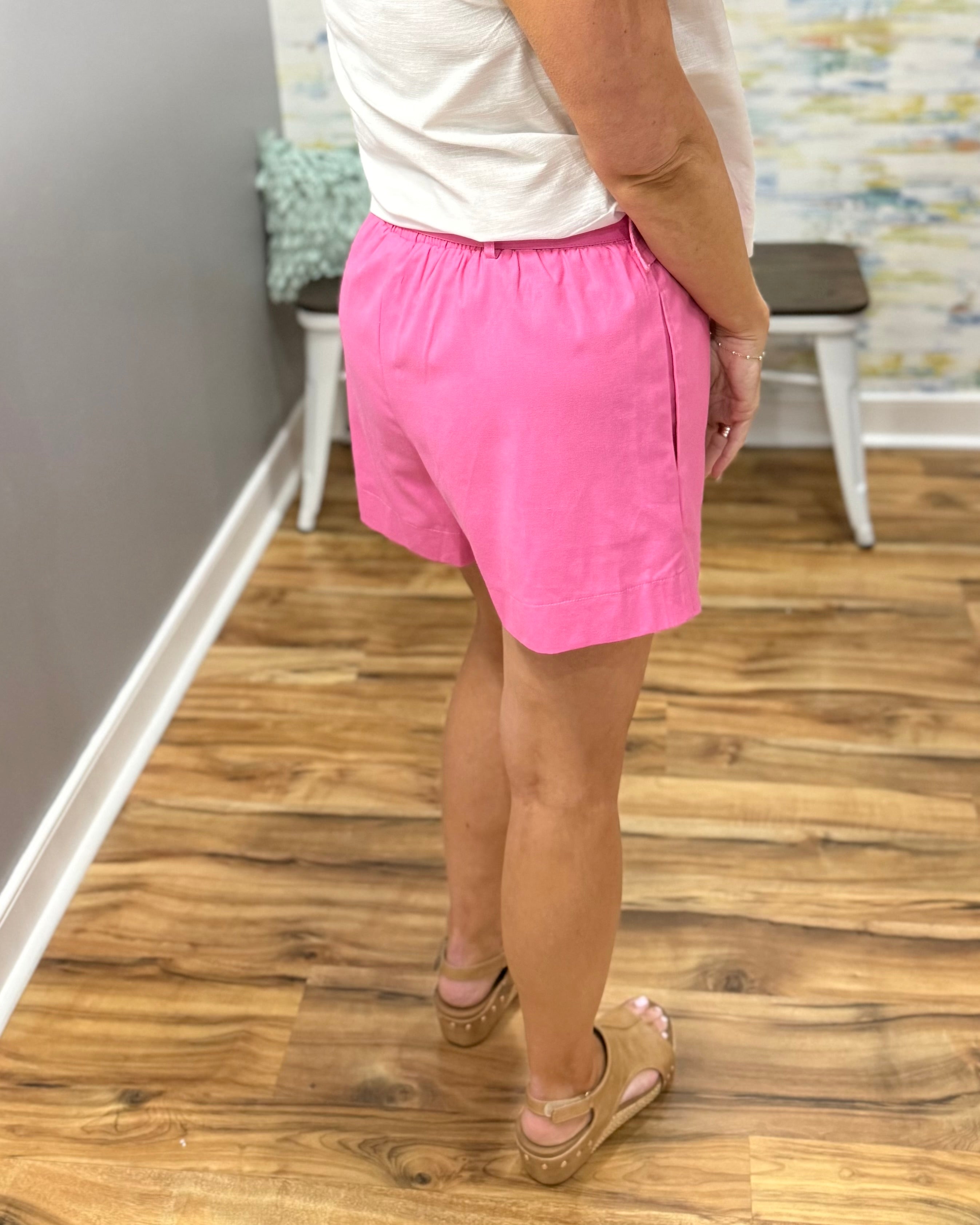 Person wearing pink shorts and a white shirt on a wooden floor.