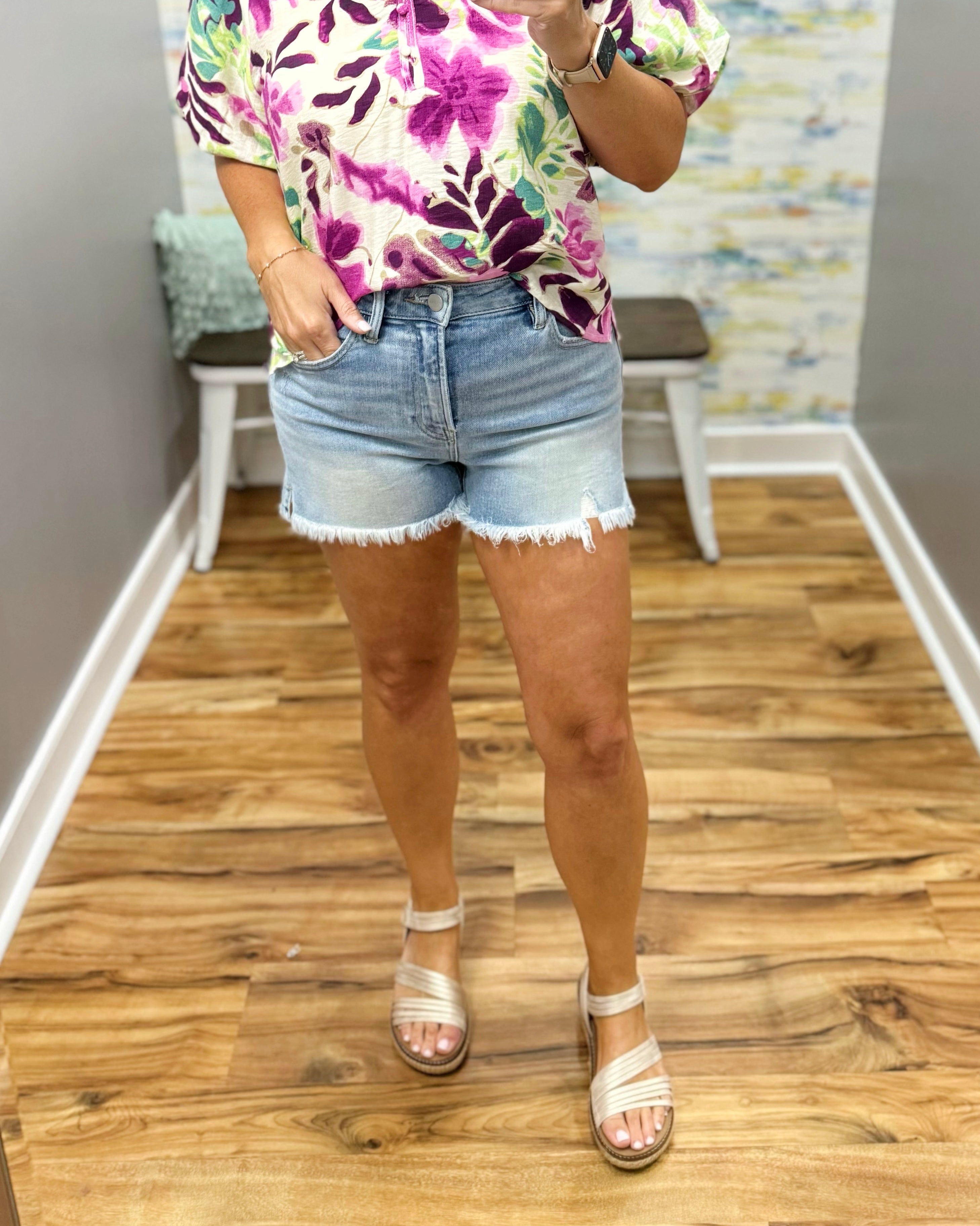 Person wearing a colorful floral shirt and denim shorts on a wooden floor.