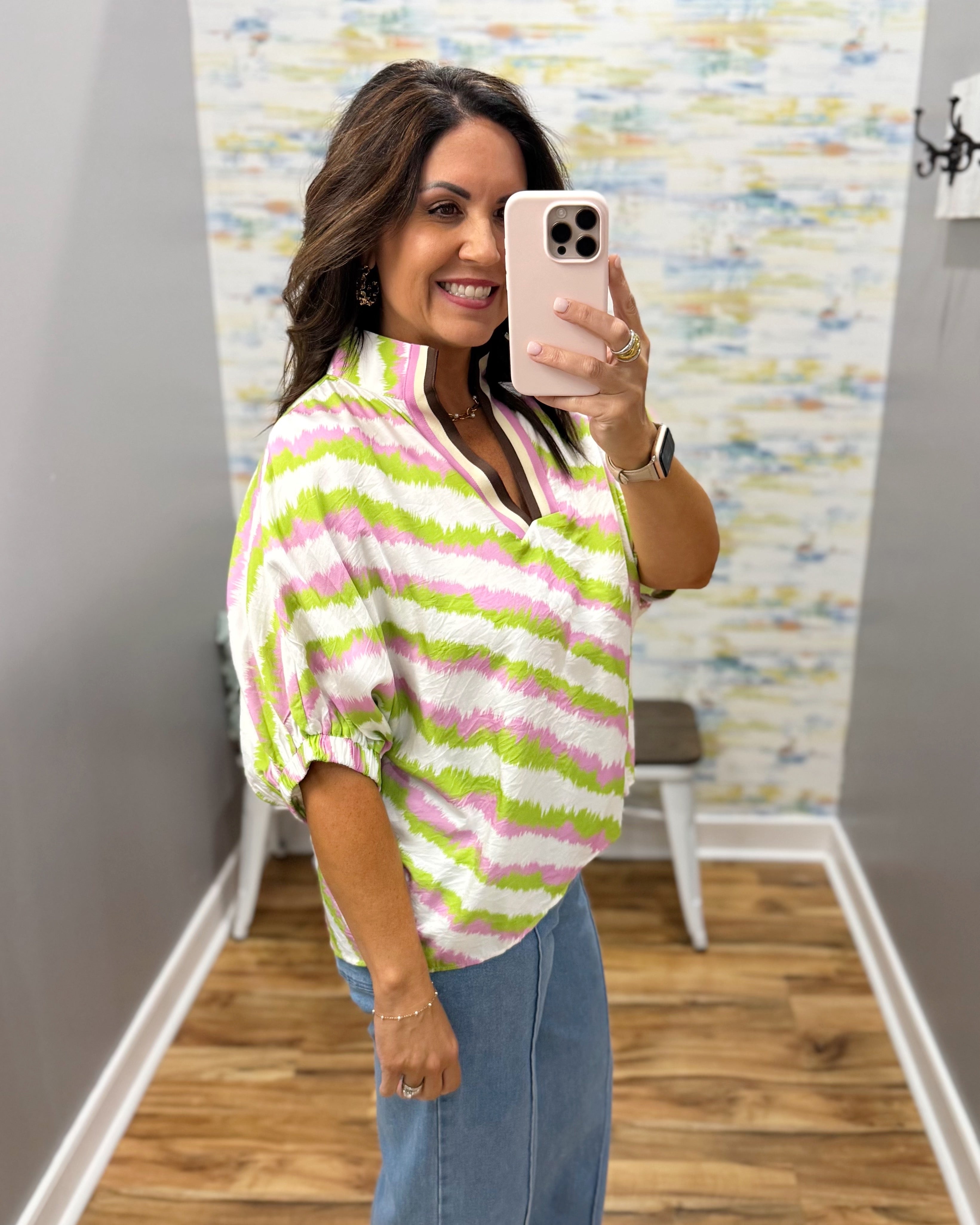 Woman taking a mirror selfie wearing a colorful striped shirt in a room with a patterned wall.