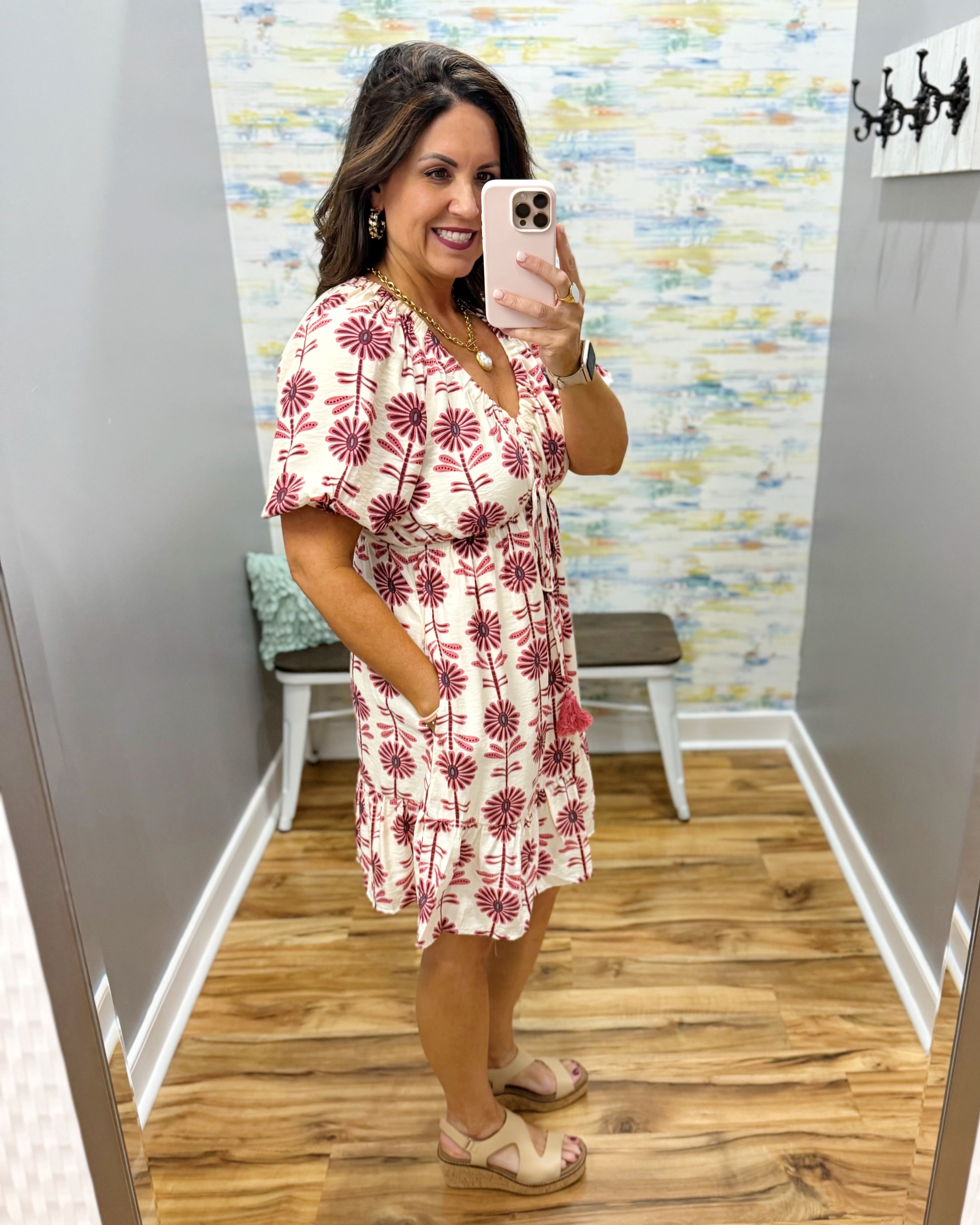 Woman taking a mirror selfie wearing a floral dress in a room with colorful wall art.