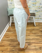 Person wearing light-colored pants standing on a wooden floor with a colorful wall in the background.