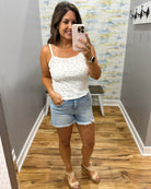 woman wearing white floral cami top with denim shorts.