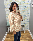 A woman takes a mirror selfie in a fitting room wearing a beige and cream zebra-print knit sweater and dark blue jeans.