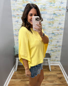 woman wearing a yellow dolman sleeve top with denim shorts.