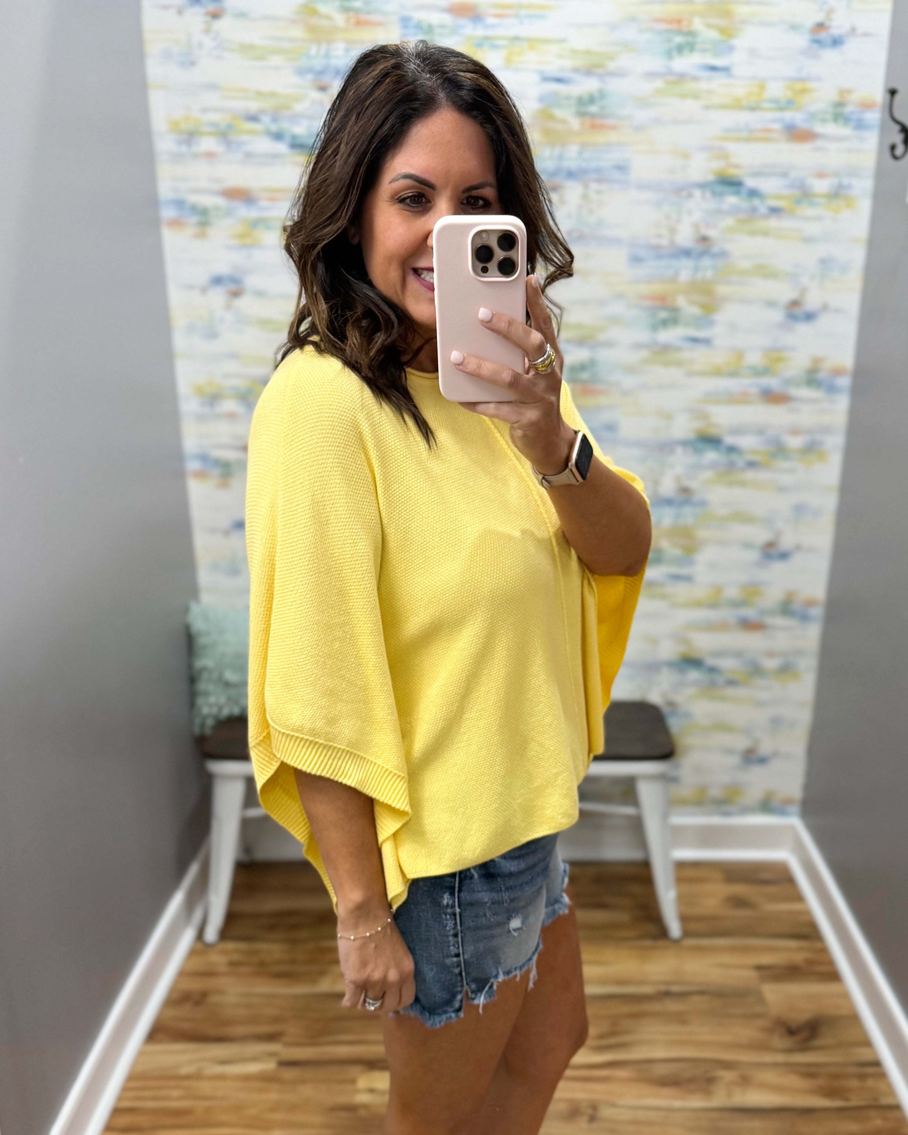 woman wearing a yellow dolman sleeve top with denim shorts.