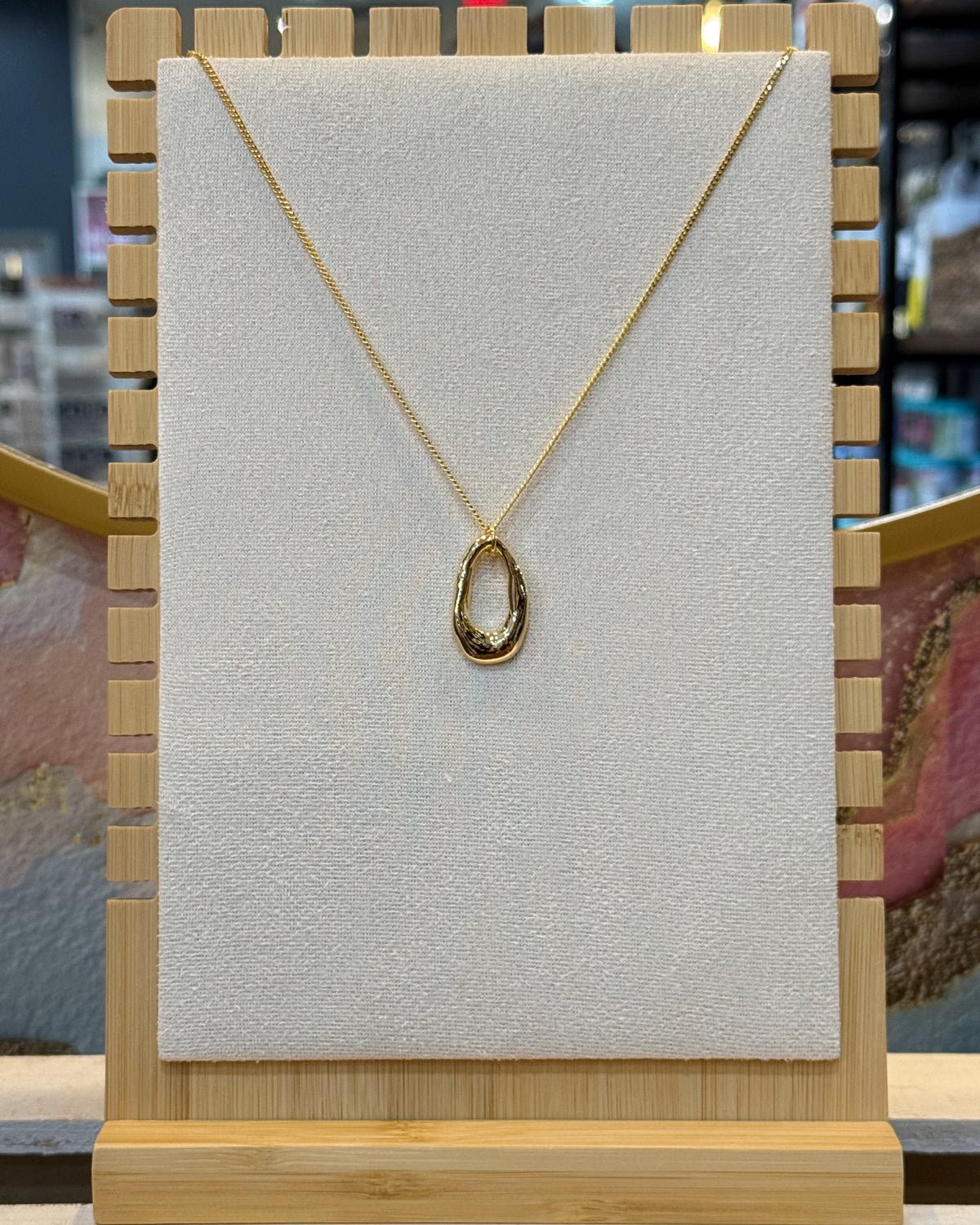 This organic oval open ring pendant necklace features a sculpted elongated oval ring with a molten wavy edge hanging from a fine gold tone chain.