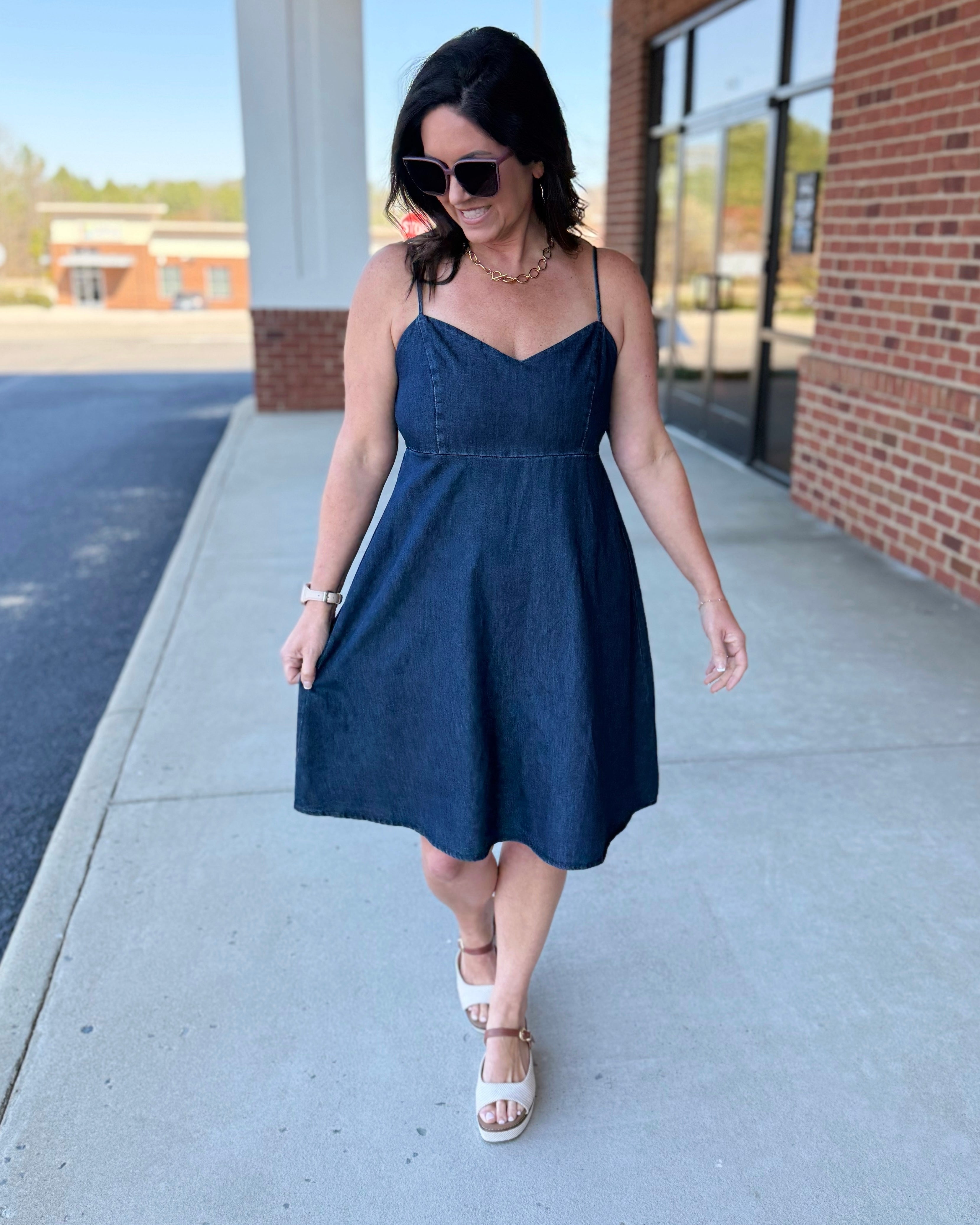Woman in a navy blue dress walking on a sidewalk.