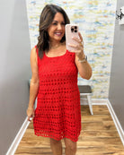 Woman taking a mirror selfie wearing a red crochet dress in a room with a colorful wall.