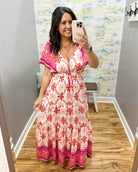 Woman taking a mirror selfie wearing a floral dress in a room with a patterned wall.