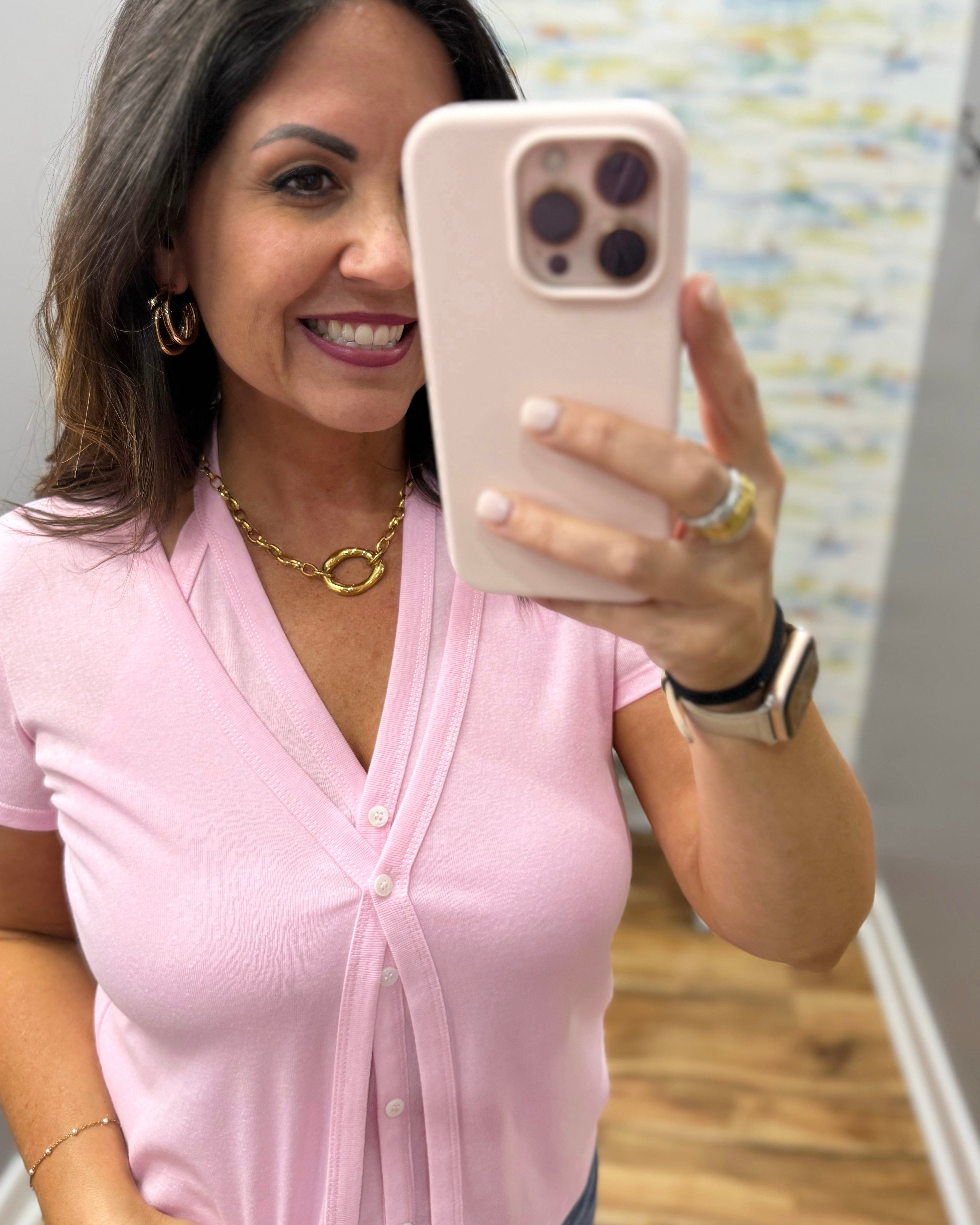 Woman in a pink shirt taking a selfie with a phone.