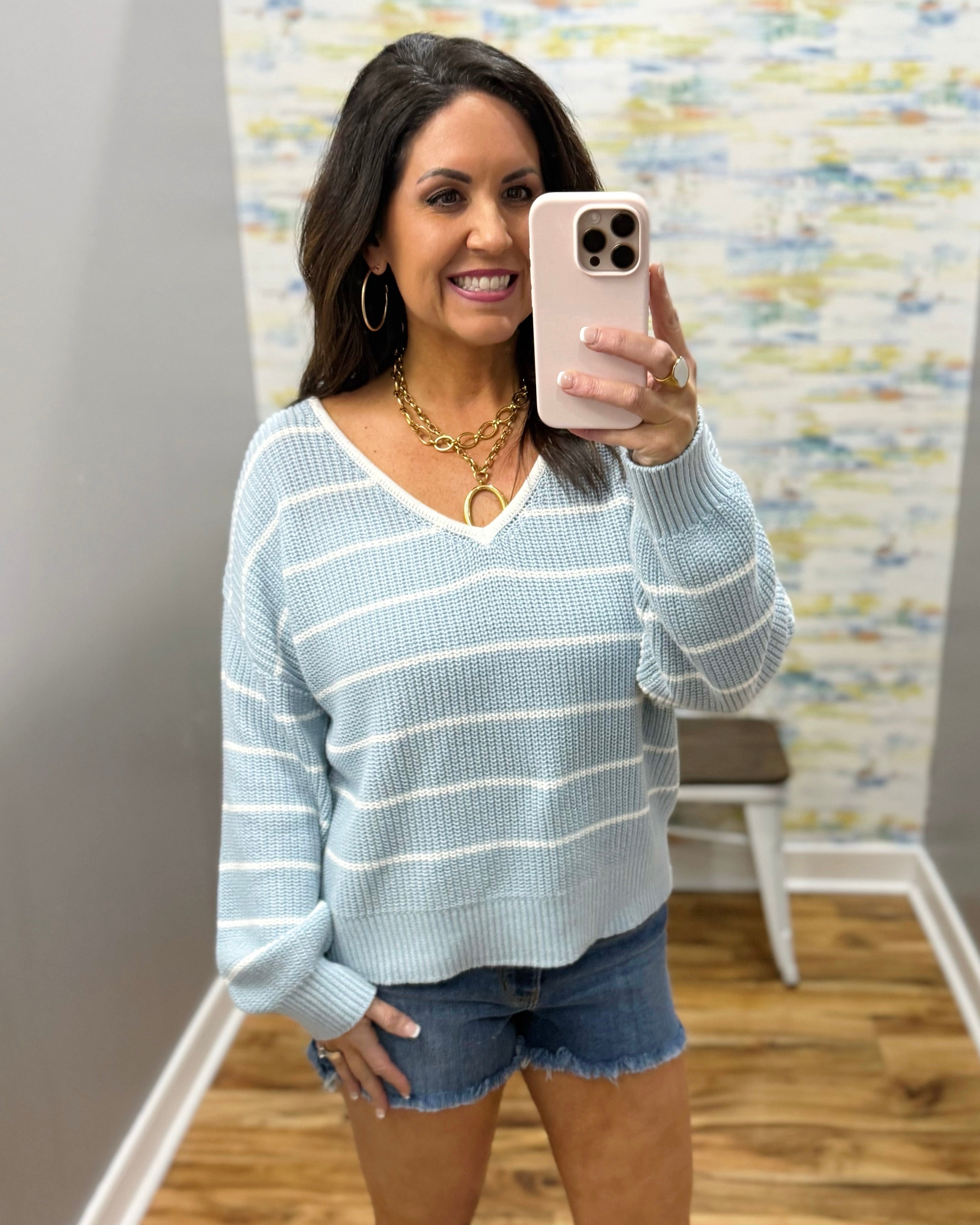 Woman wearing a light blue striped sweater and denim shorts.