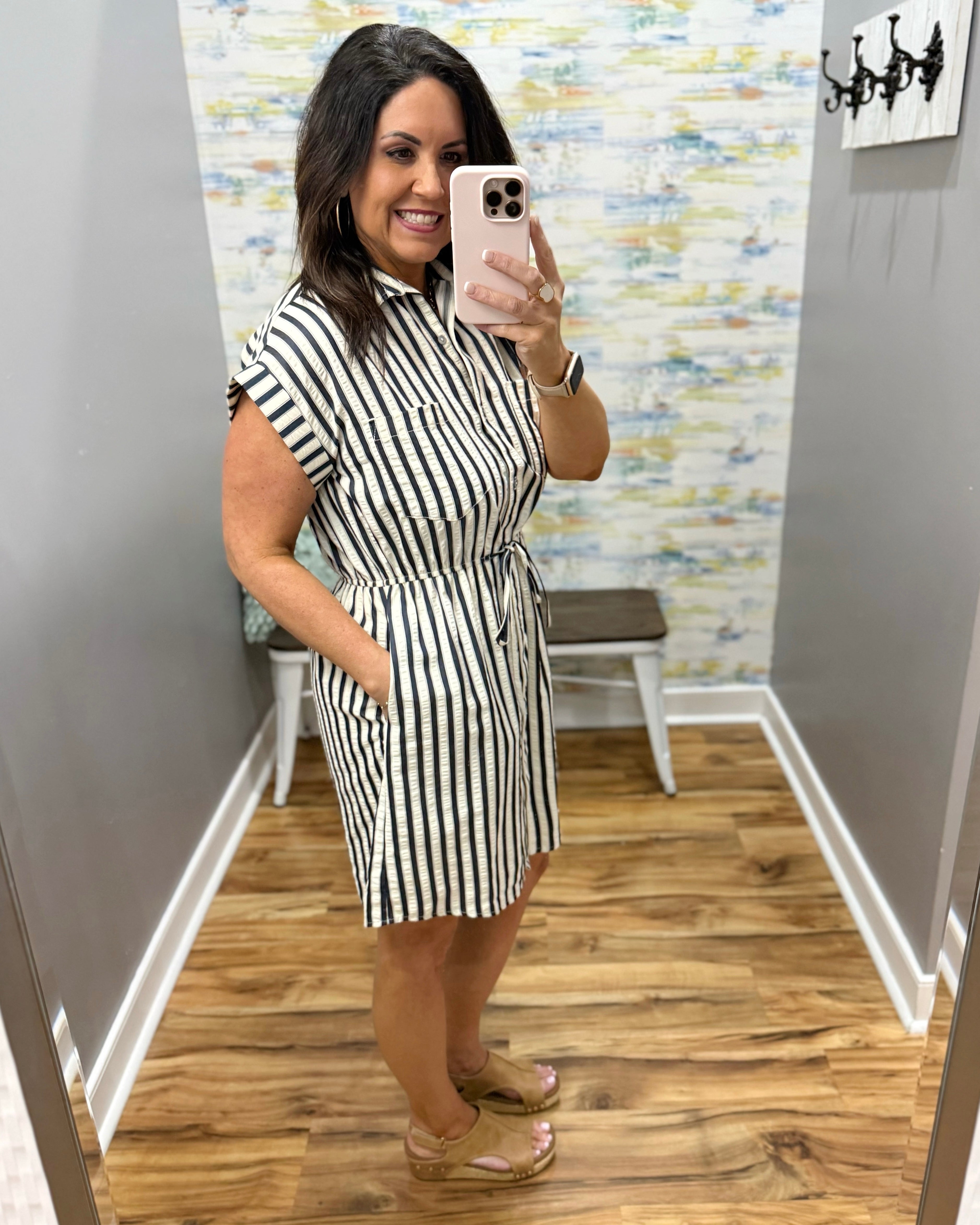 Woman wearing a black and white striped dress in a room with a patterned wall.