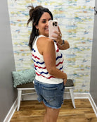 Woman taking a mirror selfie wearing a striped sleeveless top and denim shorts in a room with colorful wall art.