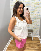 Woman wearing a white top and pink shorts in a room with a colorful wall.
