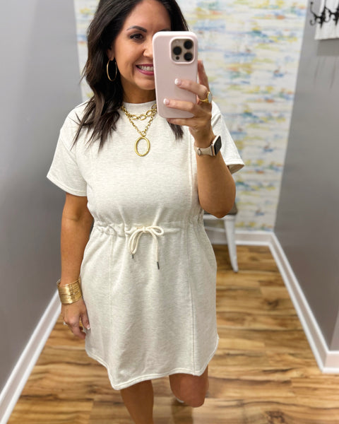 Woman wearing a neutral dress and white sneakers.