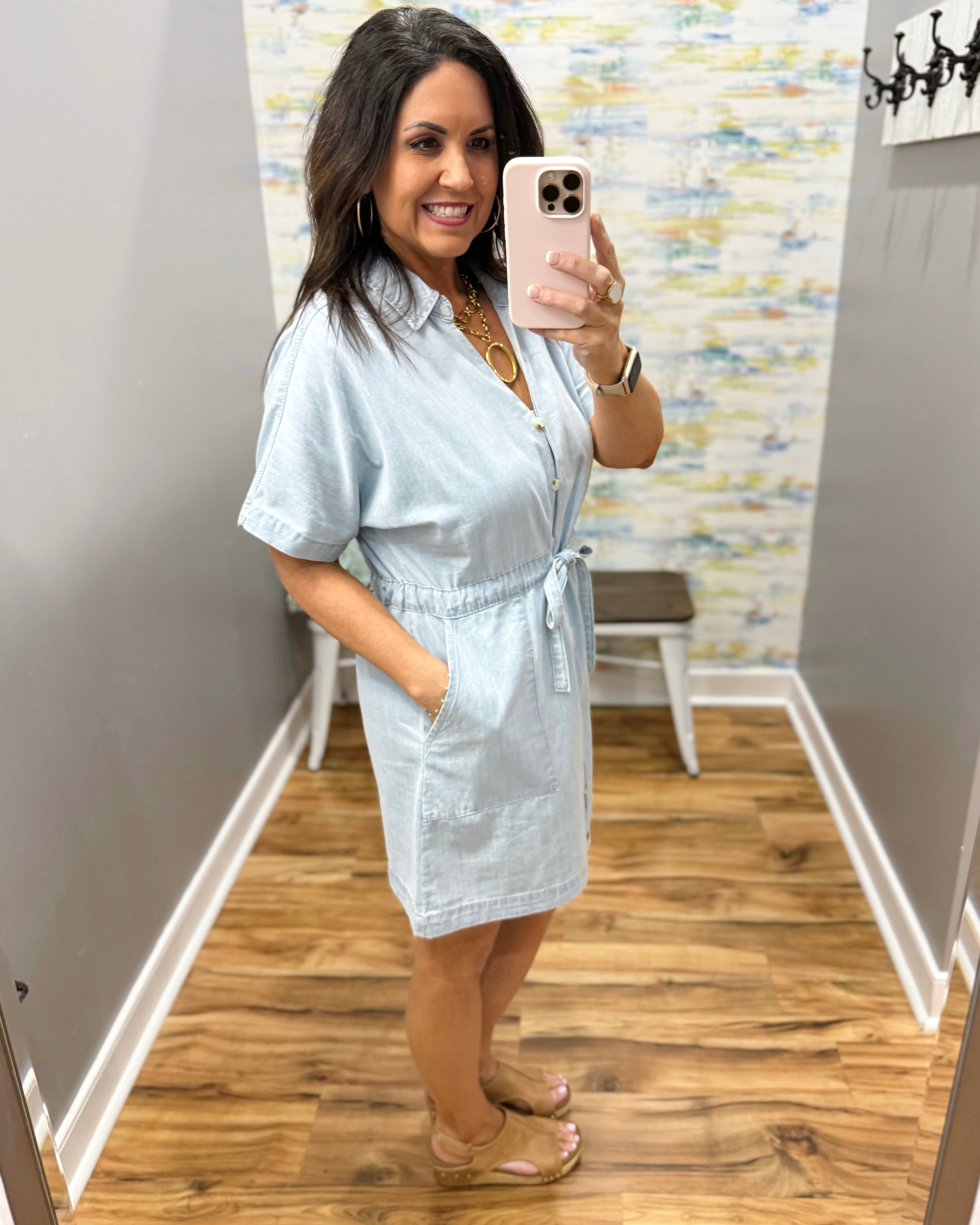 Woman wearing a light blue dress in a room with patterned wallpaper.