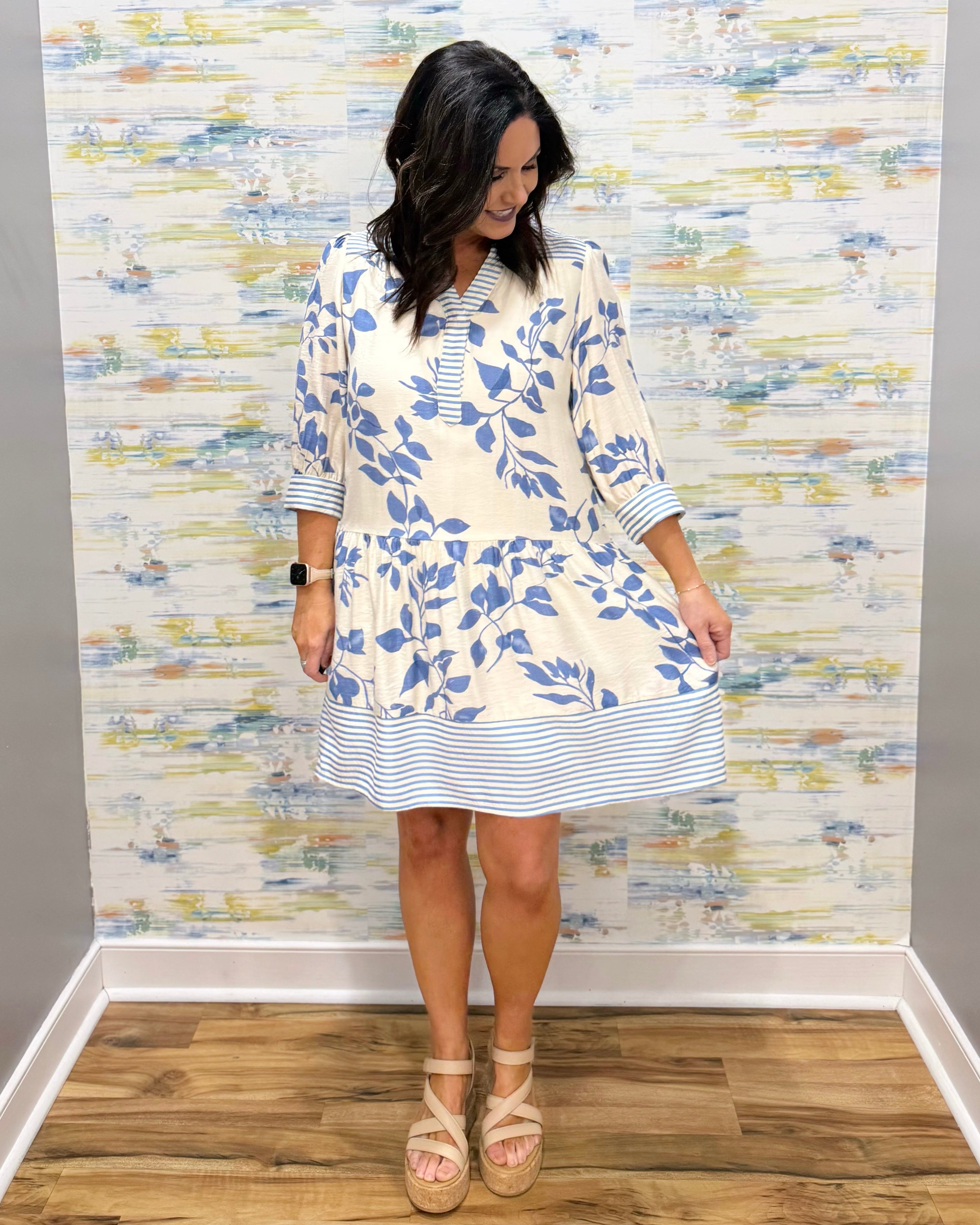 Woman wearing a blue floral dress against a patterned wall.