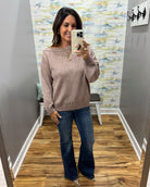 A woman takes a mirror selfie in a fitting room wearing a dusty rose off-the-shoulder knit sweater and dark blue flare jeans.