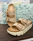 Beige sandals with white soles on a wooden surface with decorative background